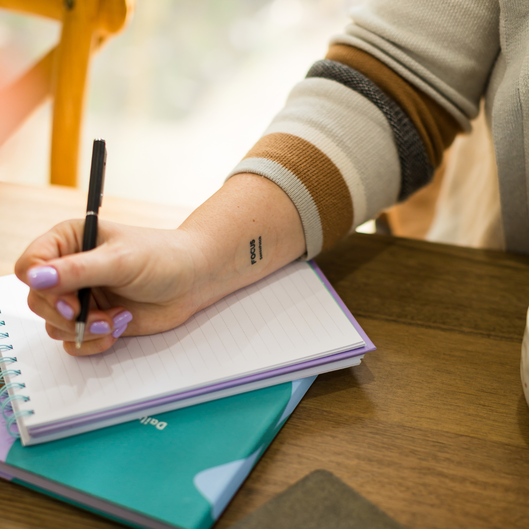 Woman writing in a notebook, showcasing the wellness patch bundle on her arm for focus, energy, and multivitamin support.
