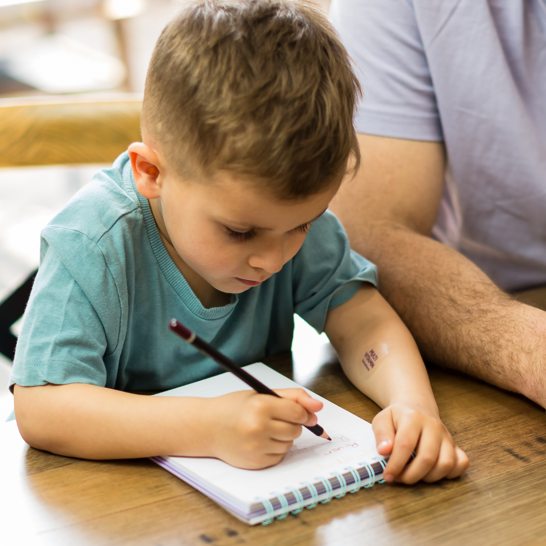 Child focused on writing in a notebook while using a wellness patch bundle for support.