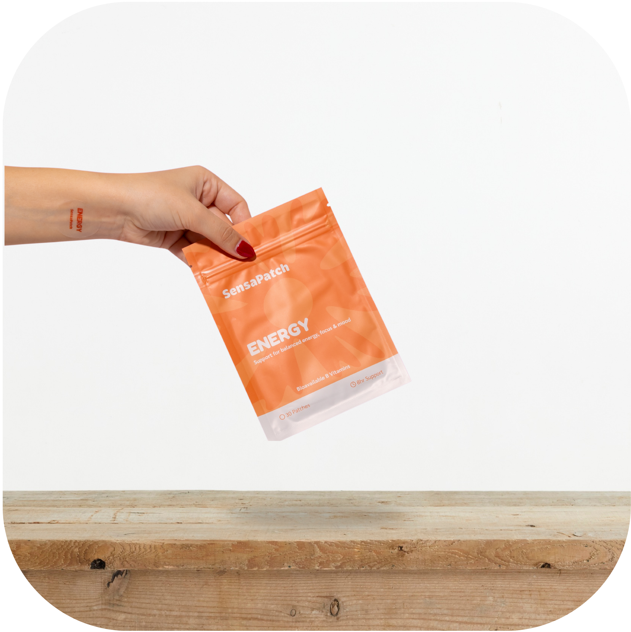 Hand holding a SensaPatch Energy package above a wooden cutting board on a white background